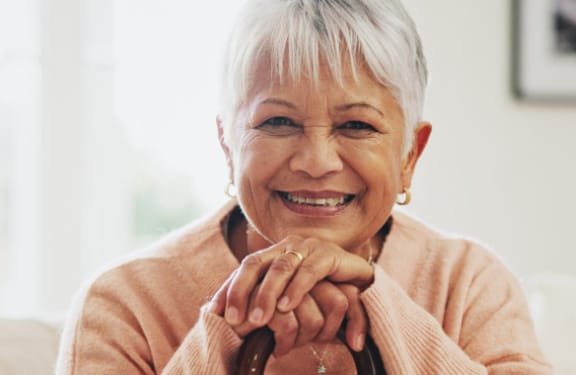 Older woman with both hands and her chin on a cane